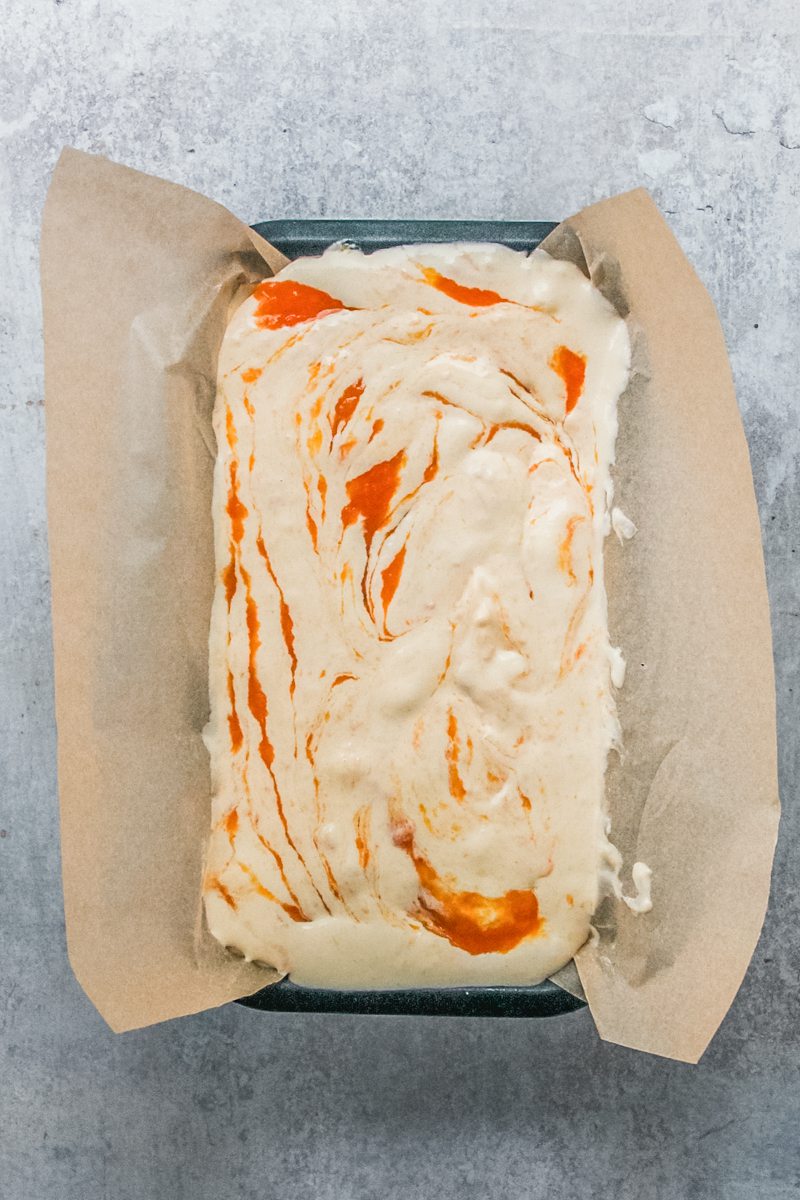 Roasted peach semifreddo sits in a lined metal loaf tin on a gray surface.