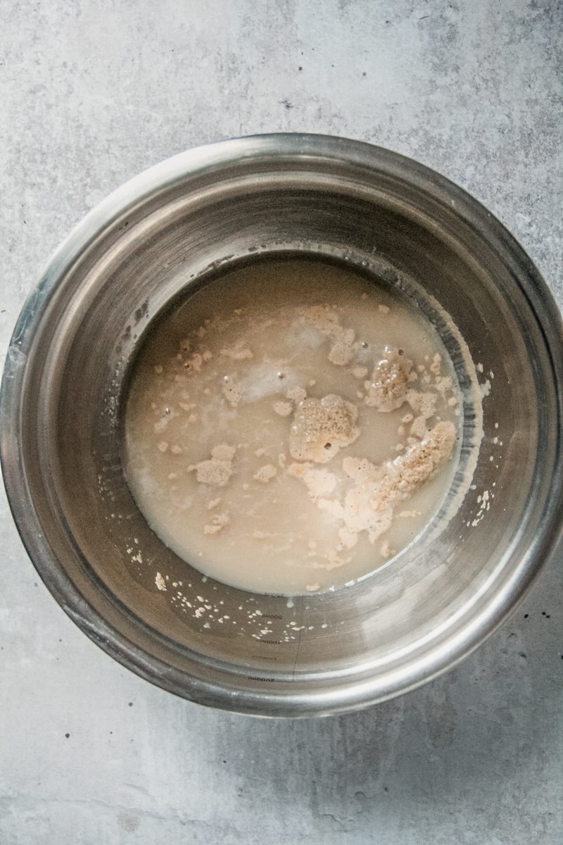 Bloomed yeast and water sit in a stainless steel bowl on a gray surface.