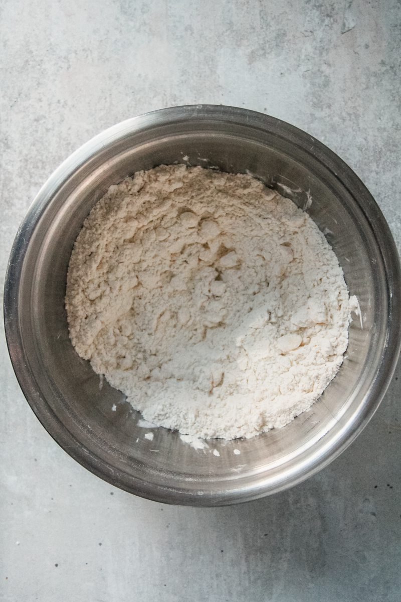 Butter tart dough ingredients sit in a stainless steel bowl on a gray surface.