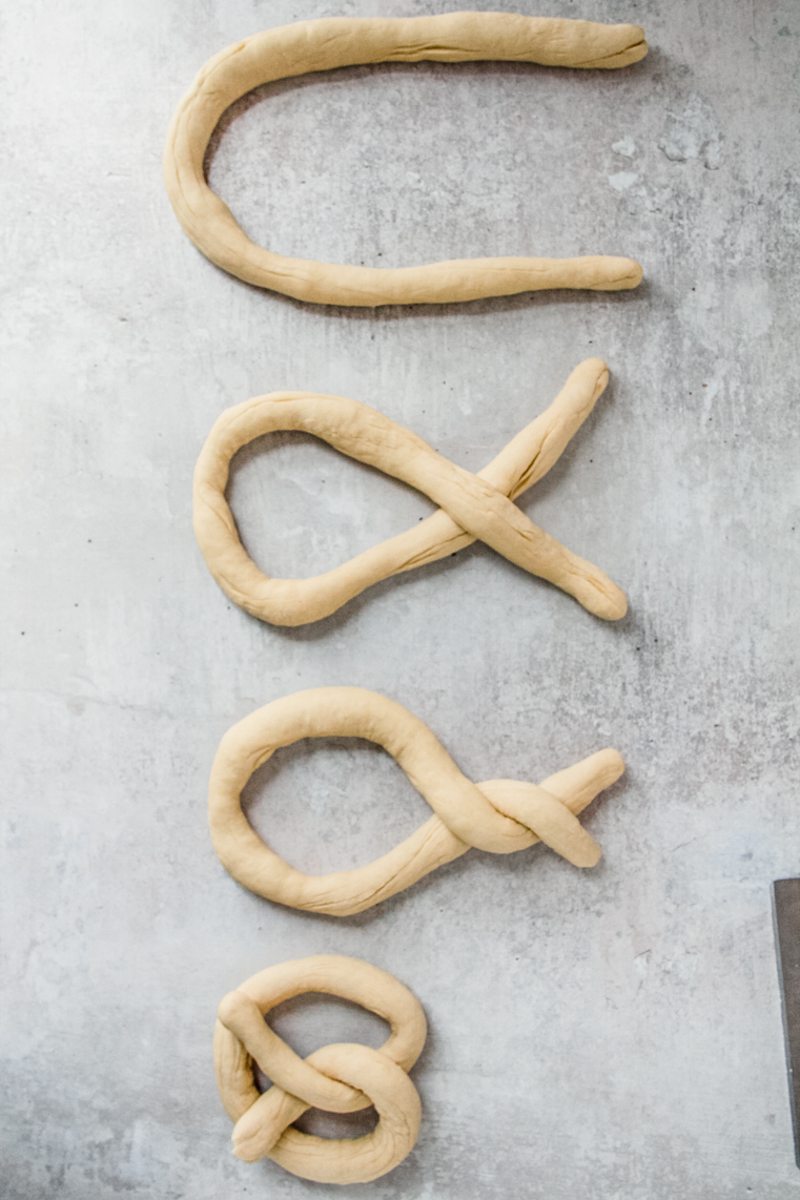 Pretzel shaped dough sit on a gray surface.