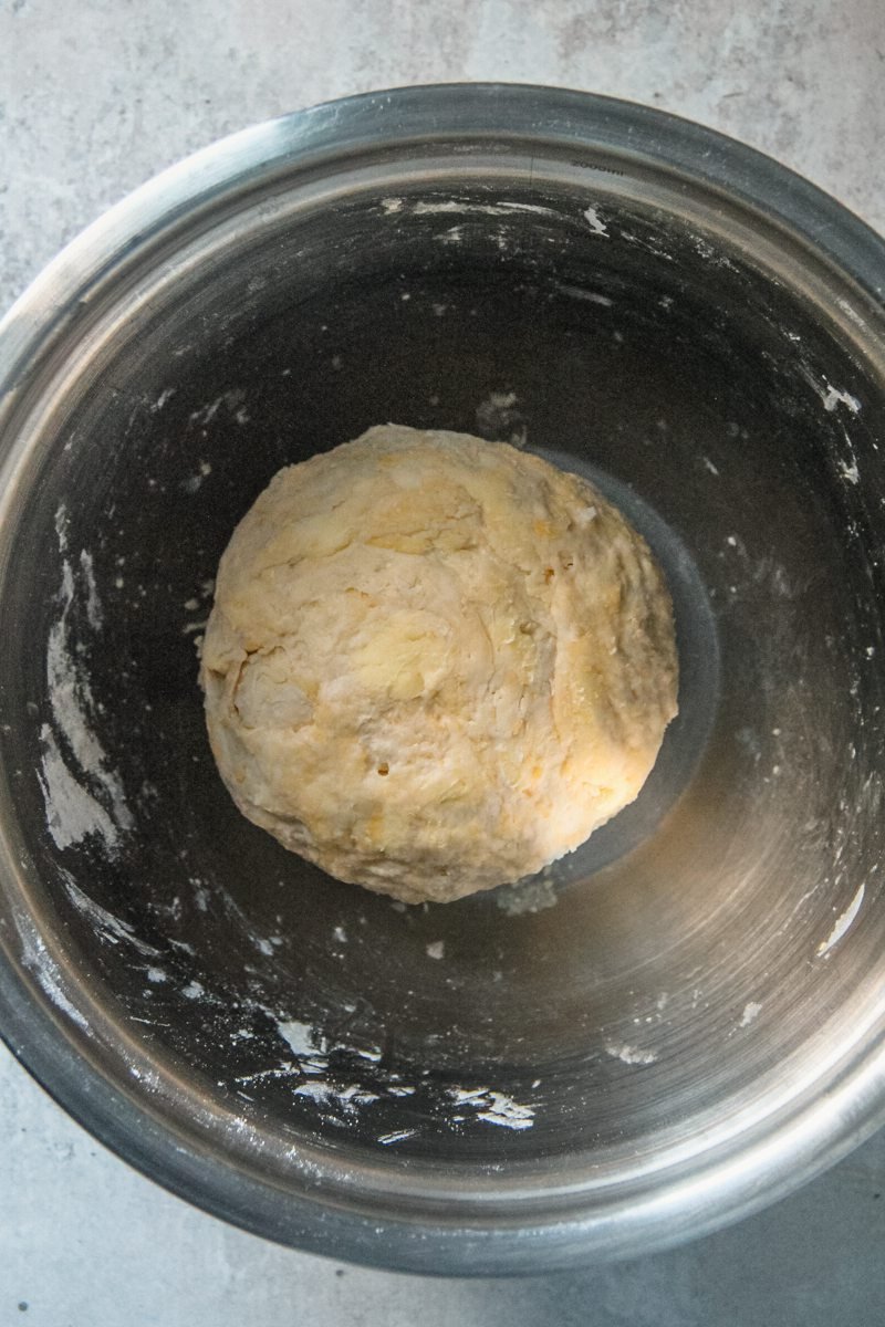 Butter tart dough sit in a stainless steel bowl on a gray surface.