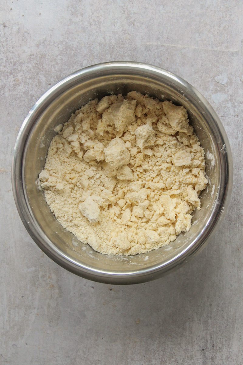 A rough crumble mixture sits in a round stainless steel bowl on a gray surface.