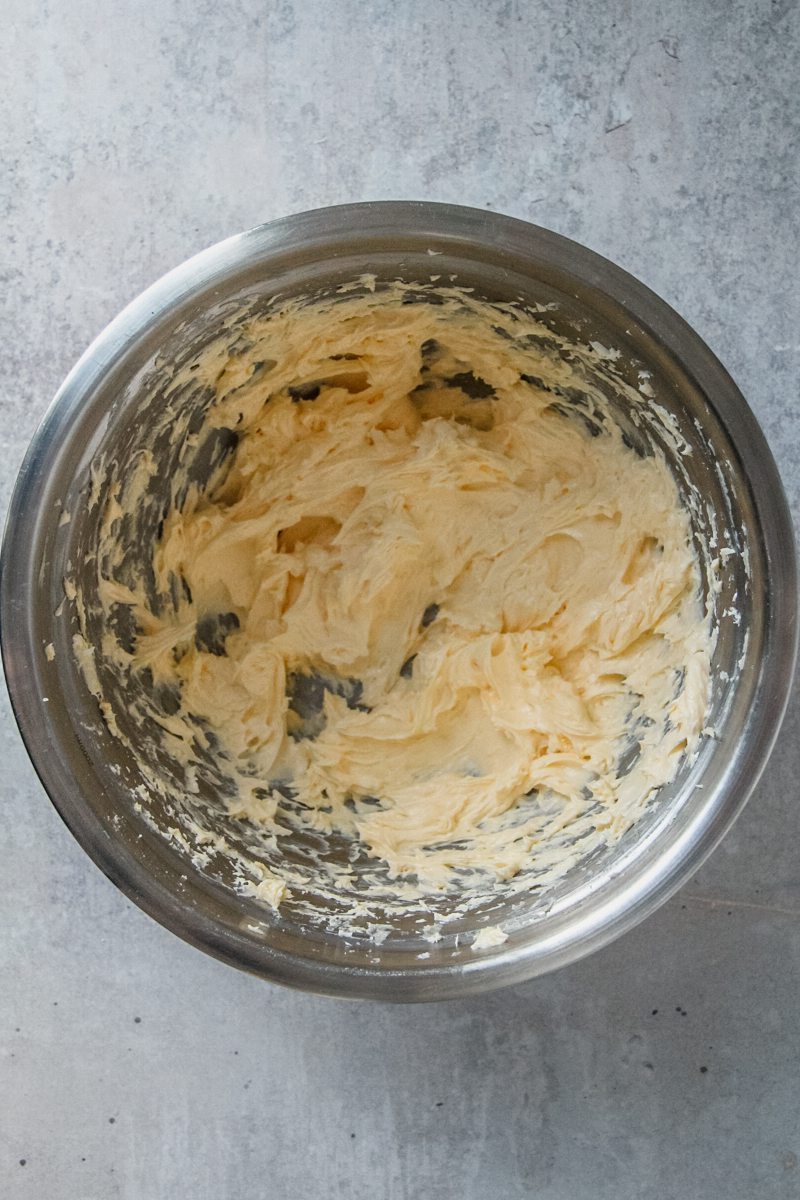 Whipped butter and egg sit in a stainless steel bowl on a gray surface.