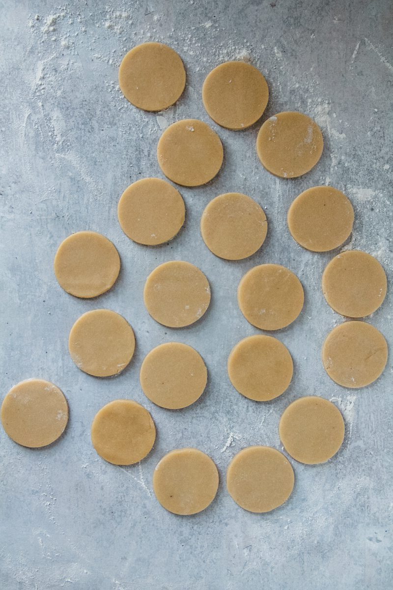 Biscochito cookie dough sits cut out in circles on a gray and lightly floured surface.