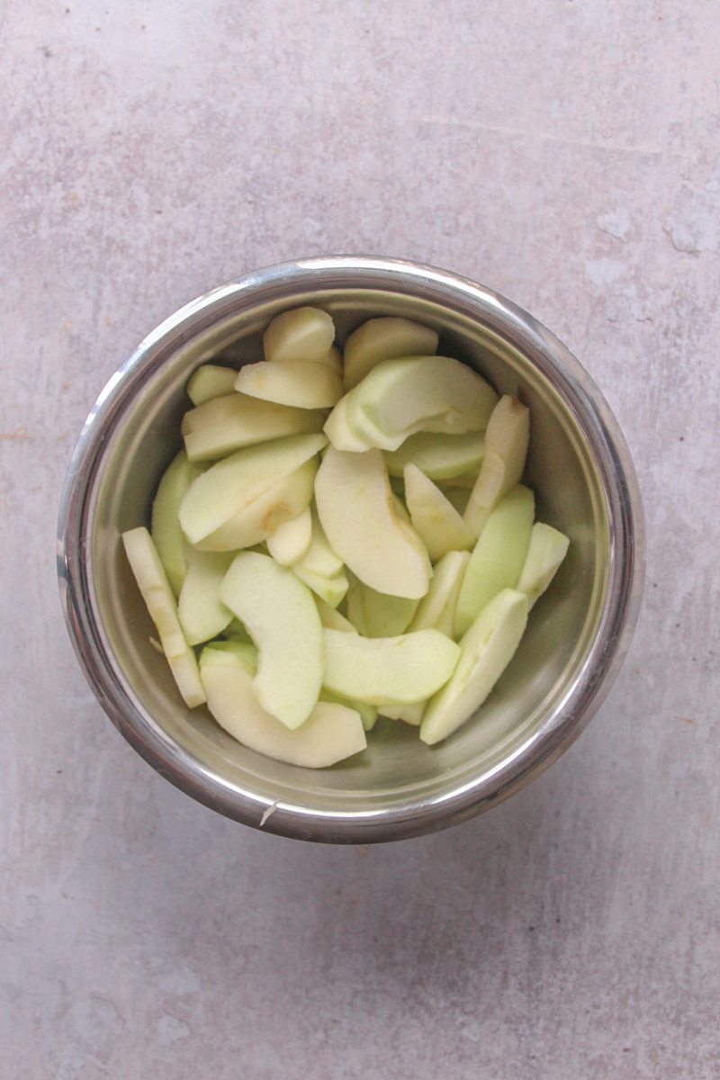 Slices of apple sit in a stainless steel bowl on a gray surface.