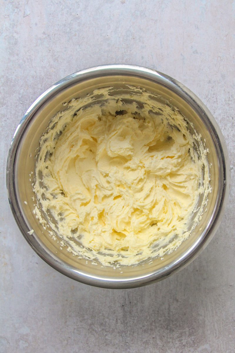 Whipped butter and sugar sit in a stainless steel bowl on a gray surface.