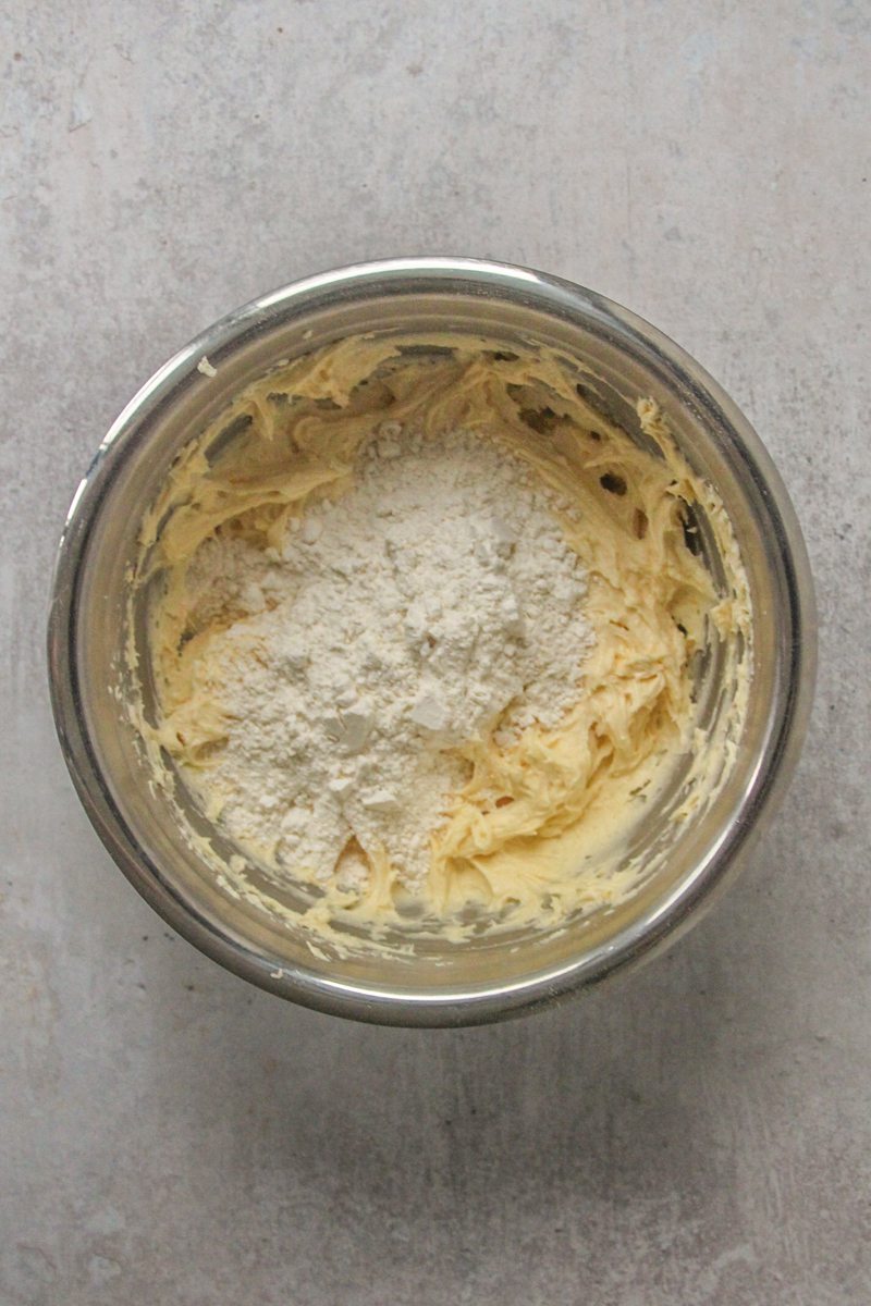 Dry ingredients sit on top of whipped cake batter in a stainless steel bowl on a gray surface.
