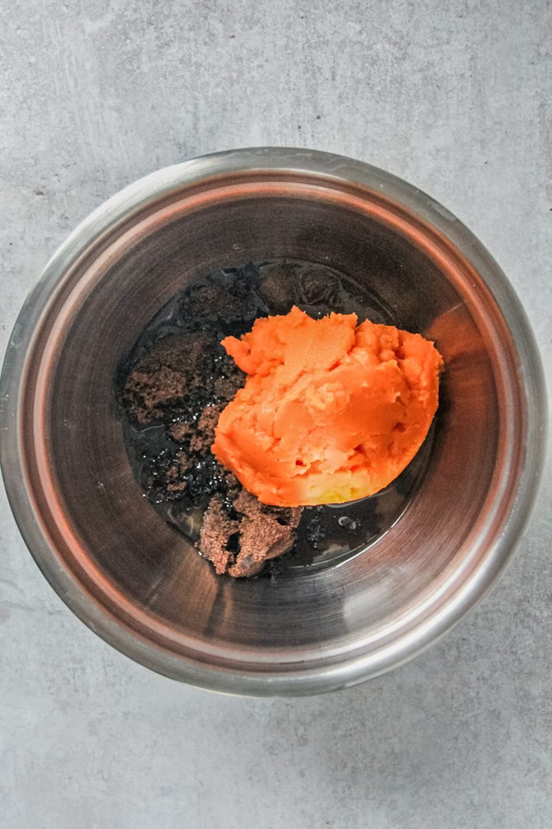 Brown sugar, oil and sweet potato puree sits in a stainless steel bowl on a gray surface.