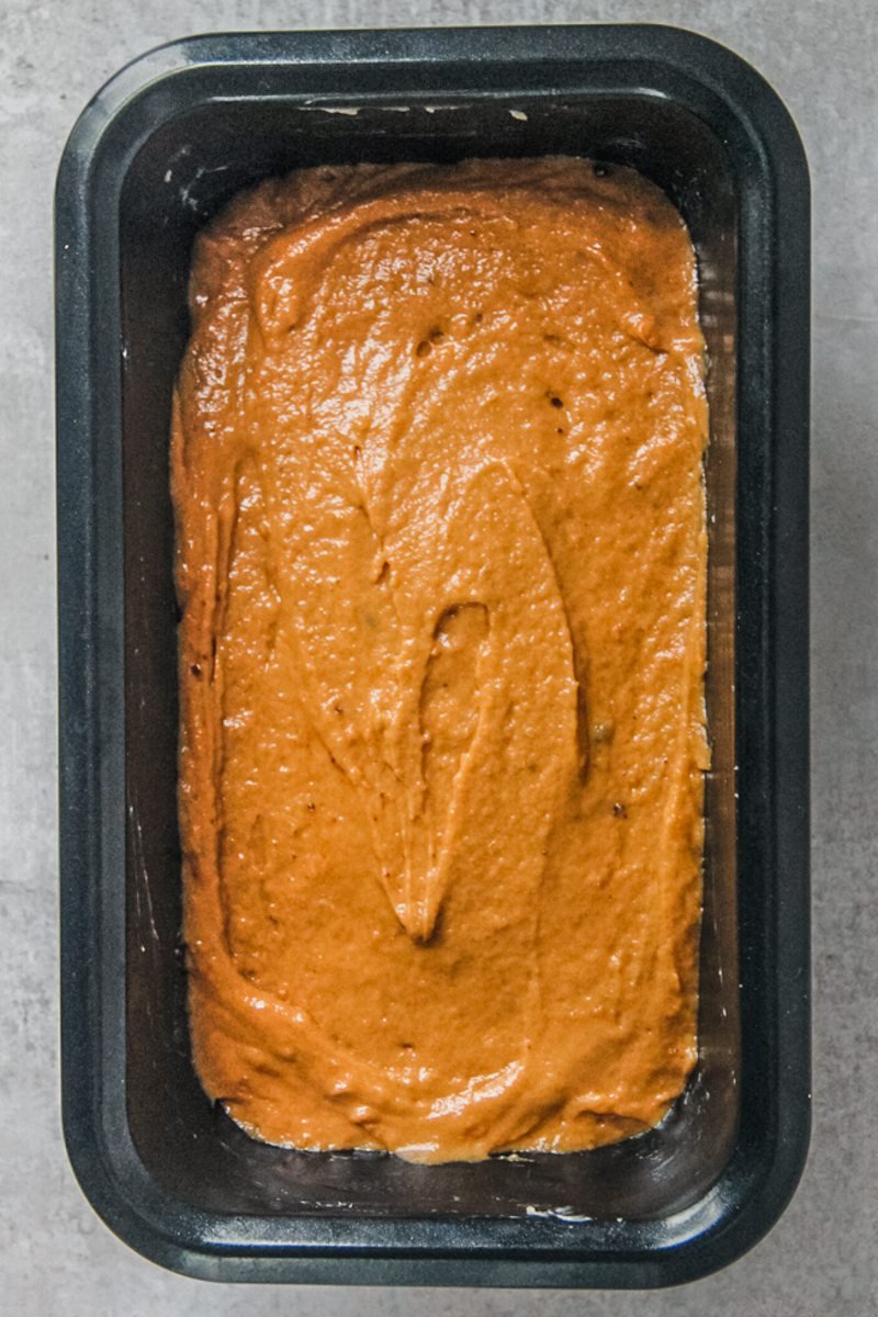 Sweet potato loaf cake sits in a metal loaf tin on a gray surface.