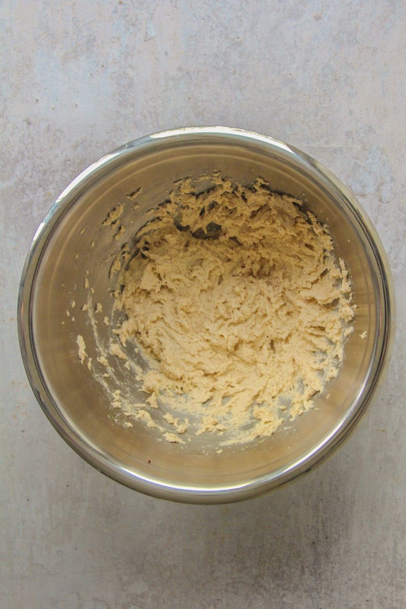 Whipped butter and sugar sit in a stainless steel bowl on a gray surface.
