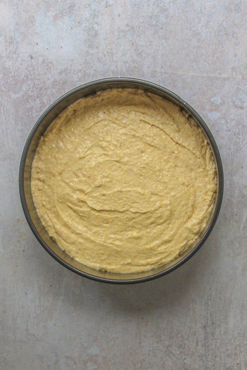 Cake batter sits in a round metal cake tin on a gray surface.