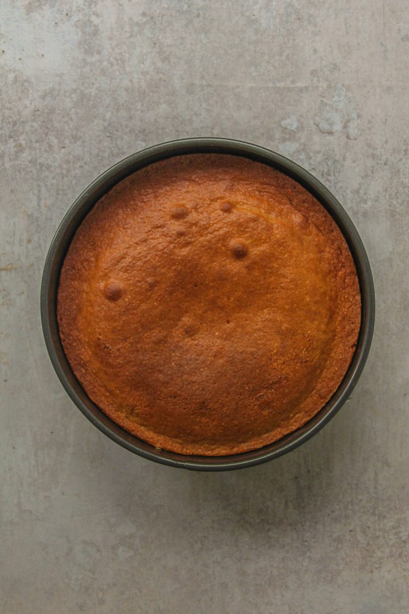 Golden cake sits in a round metal cake tin on a gray surface.
