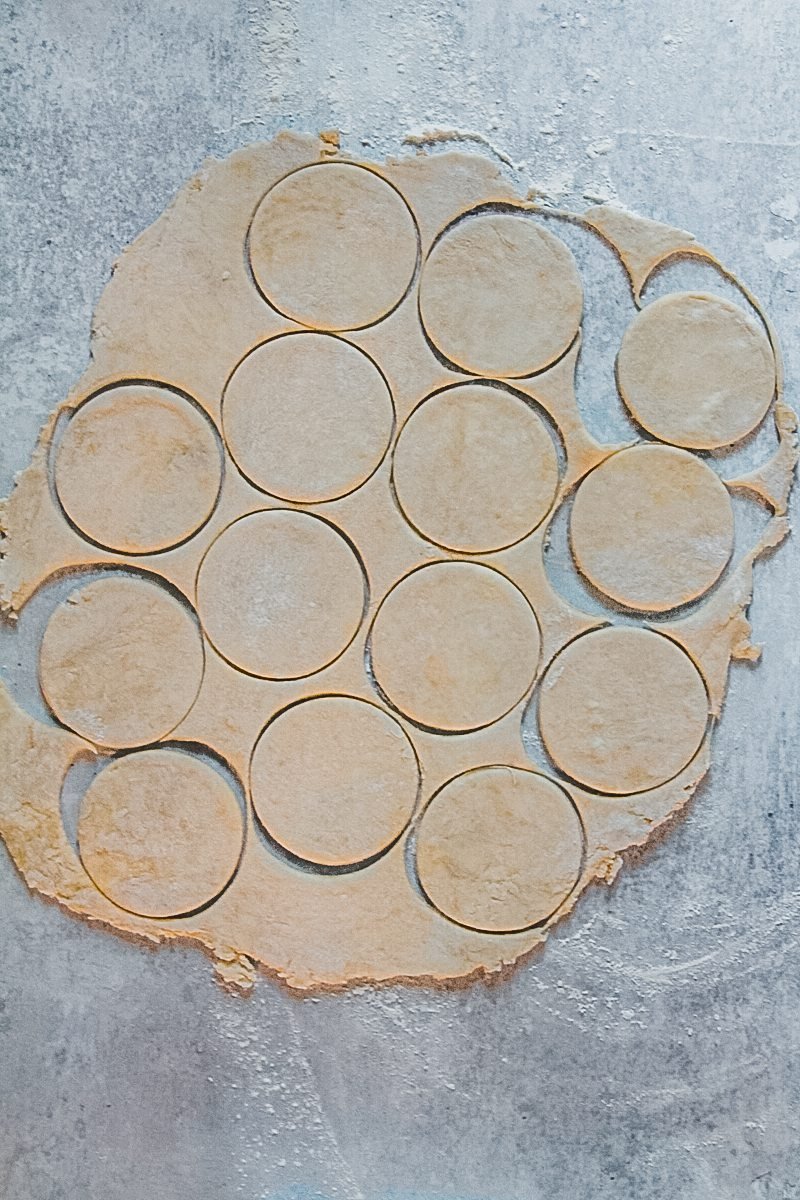 Butter tart pastry dough sits with circles cut out on a gray surface.