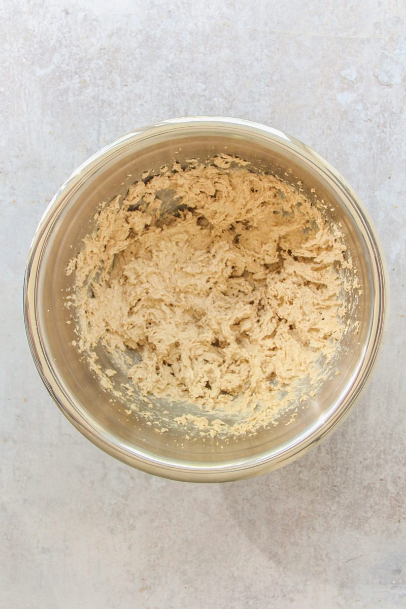 Whipped brown butter and sugar sit in a stainless steel bowl on a gray surface.