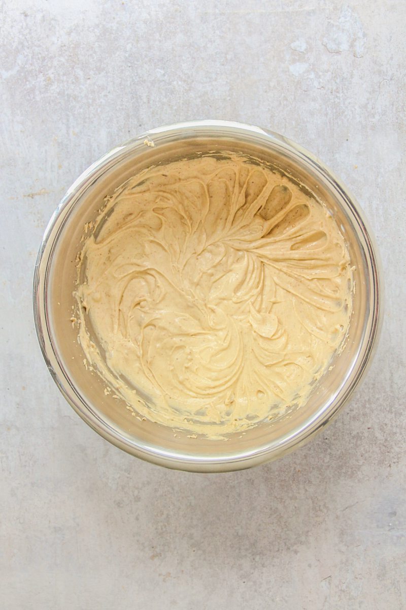 Whipped pale cake ingredients sit in a stainless steel bowl on a gray surface.