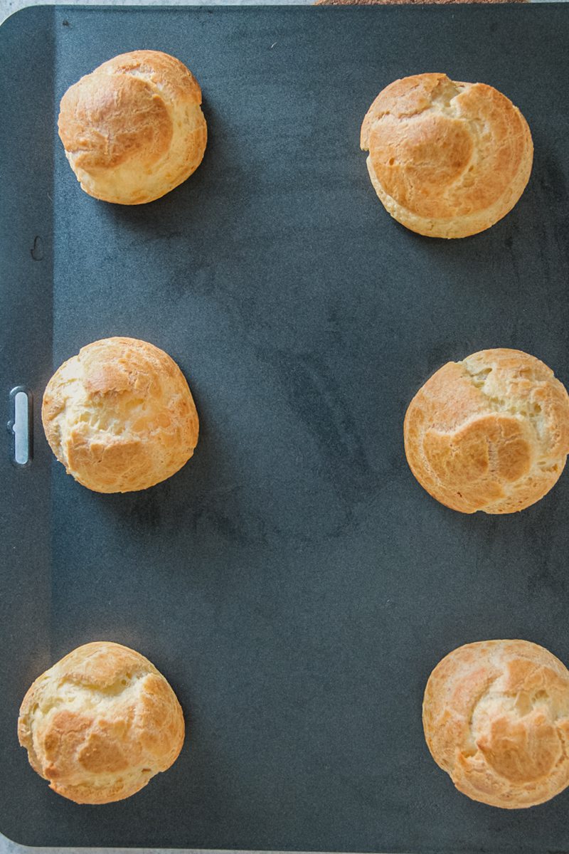 Baked choux pastries sit on a baking tray.