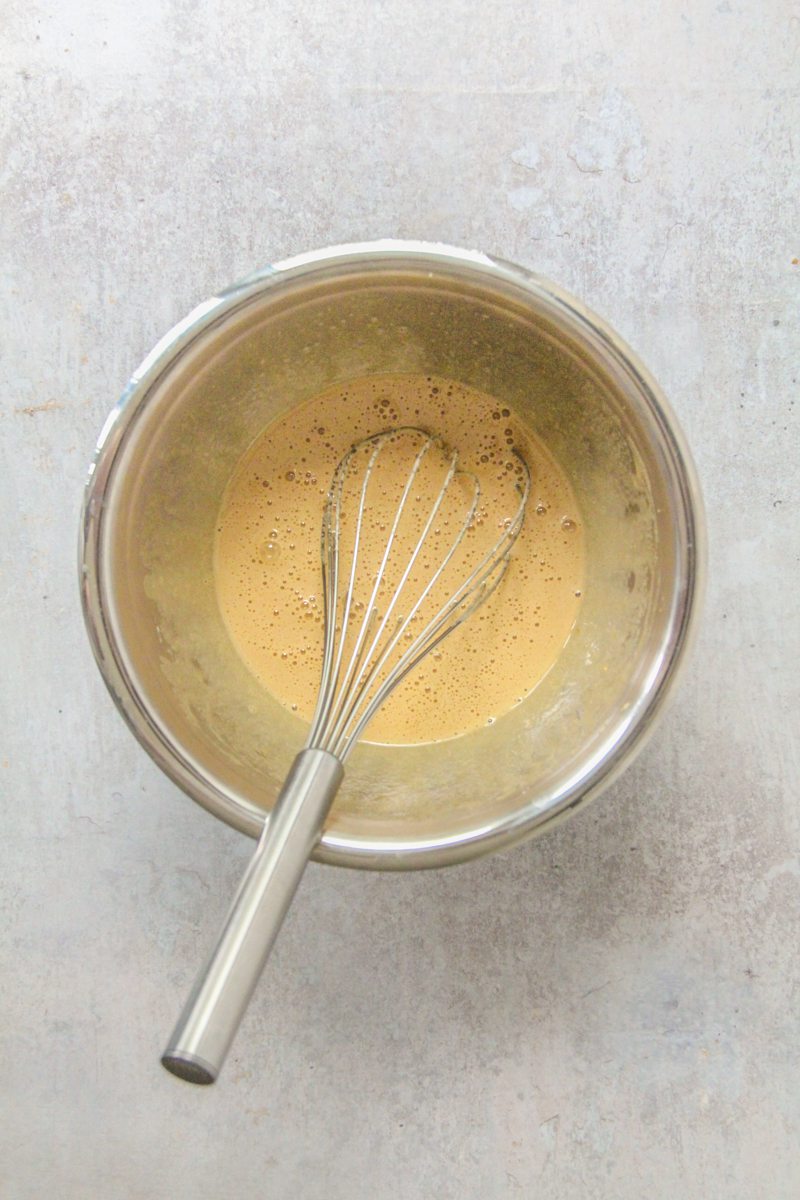 Whipped sugar and eggs sit in a stainless steel bowl on a gray surface.