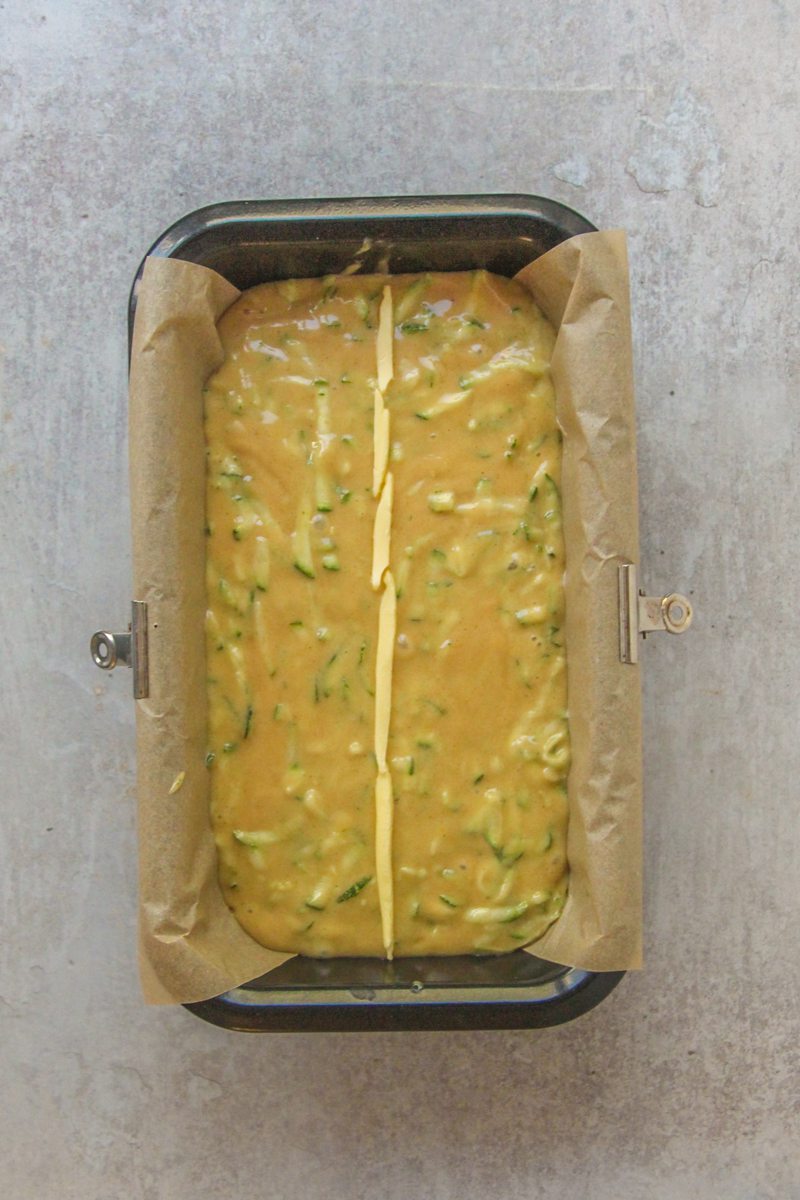 Zucchini loaf batter sits in a lined metal loaf tin on a gray surface.