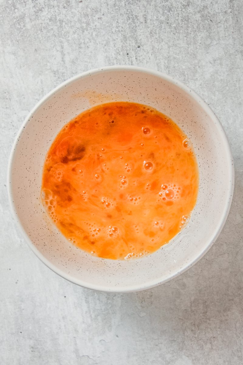 Whisked eggs sit in a white ceramic bowl on a gray surface.