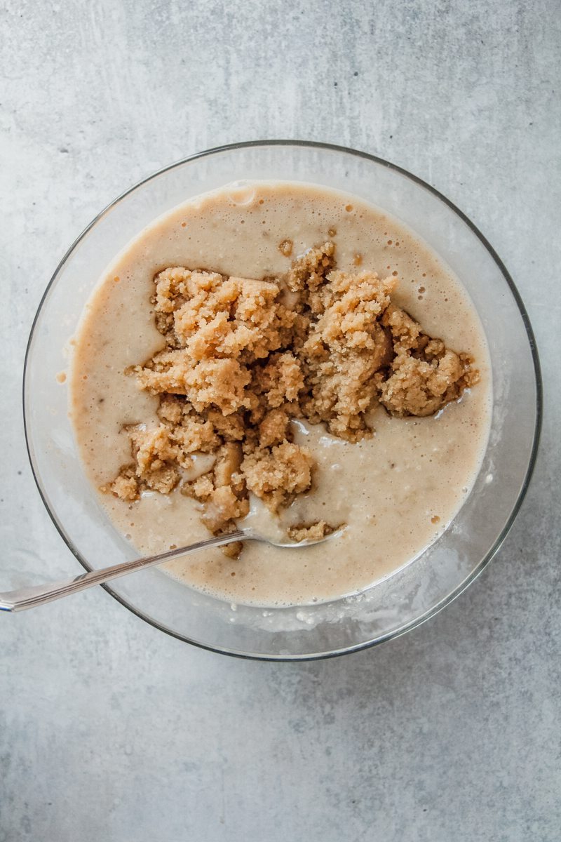 A whipped butter and sugar mixture sits on top of a porridge mixture in a glass bowl on a gray surface.