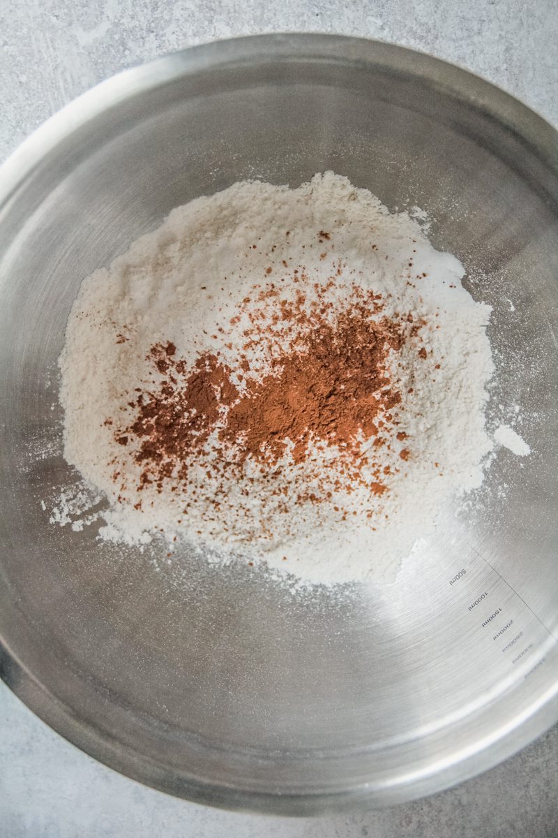 Dry ingredients and spices sit in a stainless steel bowl on a gray background.