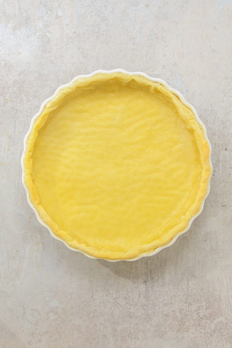 Blind baked pastry sits in a white ceramic baking dish on a gray surface.