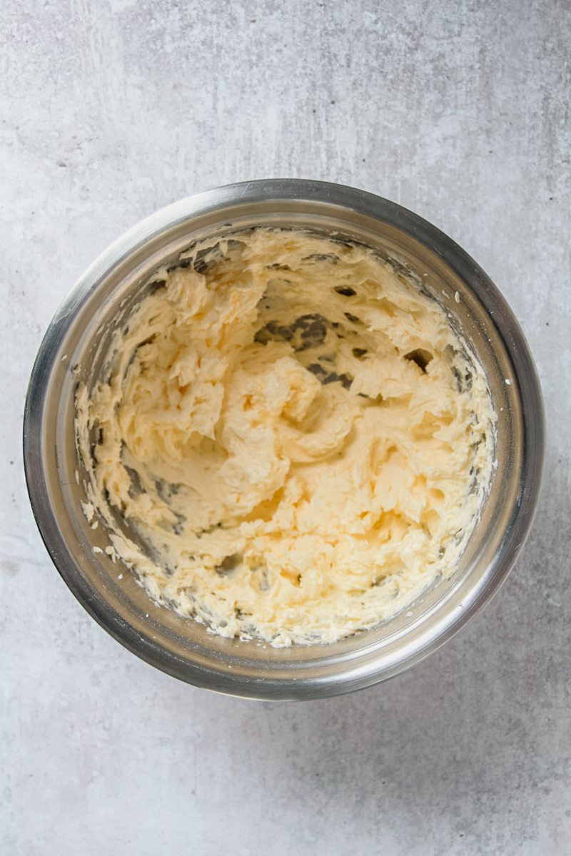 Whipped butter and sugar sit in a stainless steel bowl on a gray surface.