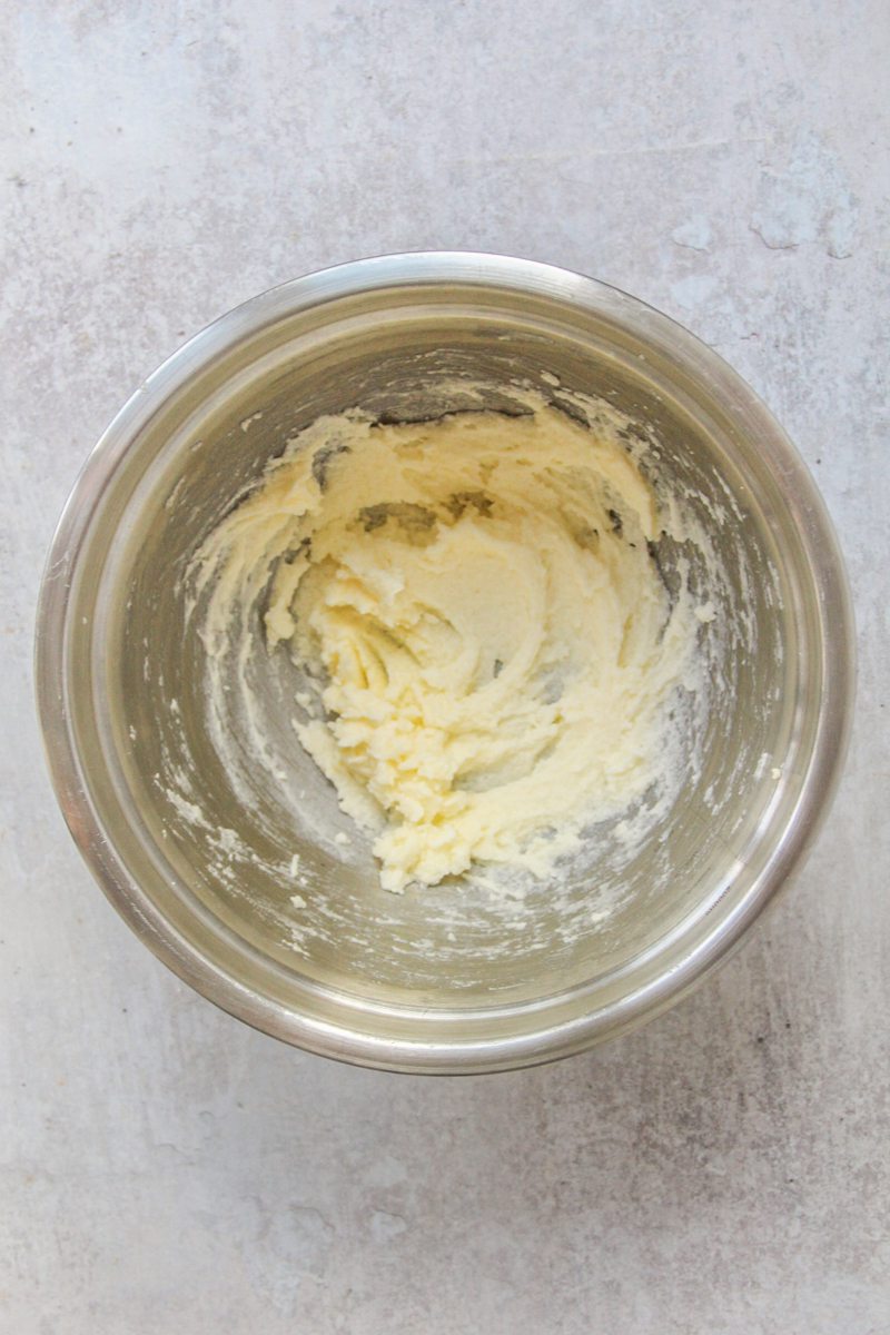 Whipped butter, sugar and water sits in a stainless steel bowl on a gray surface.