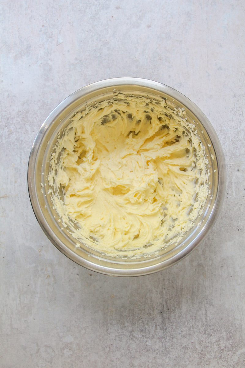Whipped butter and sugar sits in a stainless steel bowl on a gray surface.