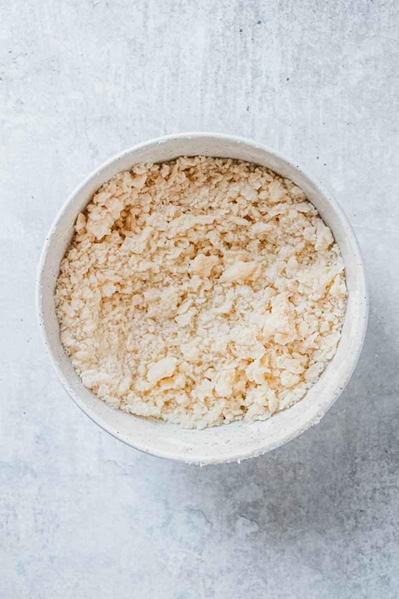 A streusel mixture sits in a white ceramic bowl on a gray surface.