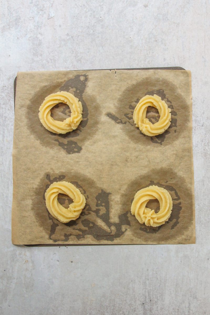 Piped butter cooke dough sits on a lined baking tray on a gray surface.