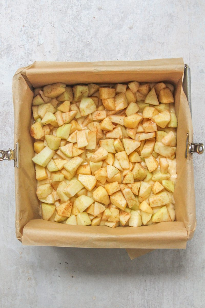 Cubed souced apples sit in a lined square tin on a gray surface.