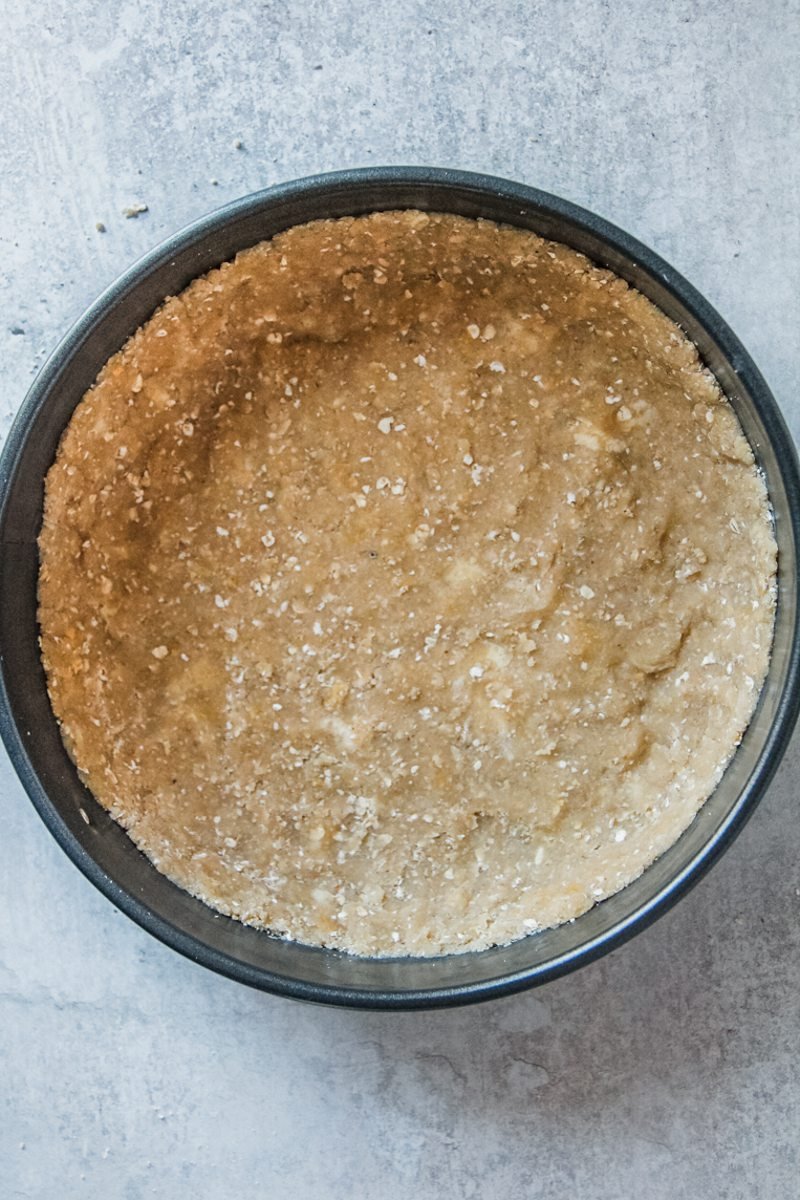 A crumble mixture sits pressed into a metal cake tin on a gray surface.