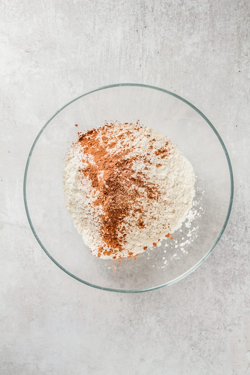 Flour and spices sit in a glass bowl on a gray surface.