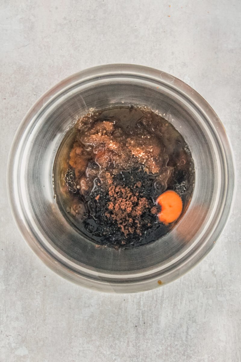 Wet ingredients for carrot cake sit in a stainless steel bowl on a gray surface.