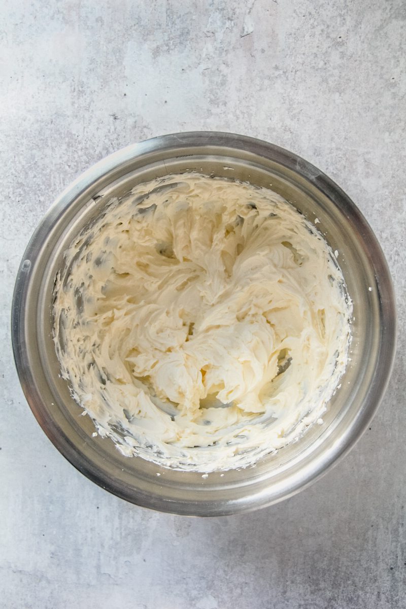 Whipped cream cheese frosting sits in a stainless steel bowl on a gray surface.