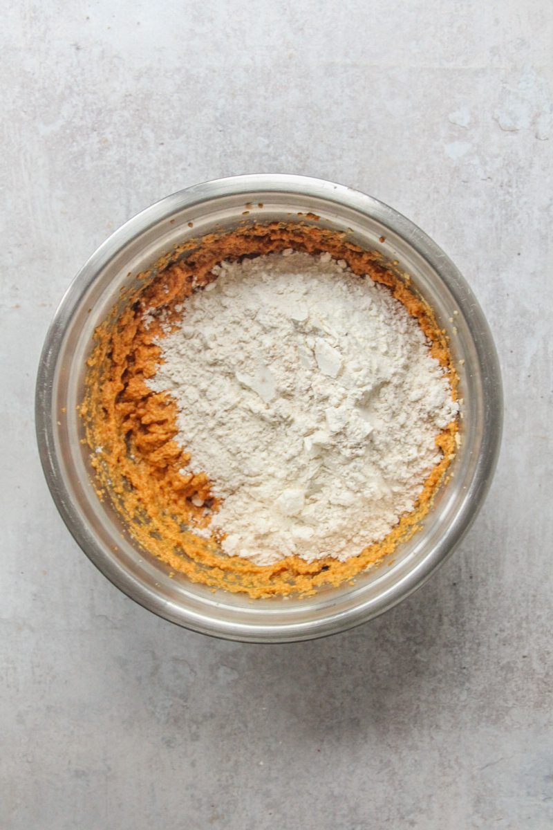 Dry ingredients sit on top of a pumpkin bread mixture in a stainless steel bowl on a gray surface.
