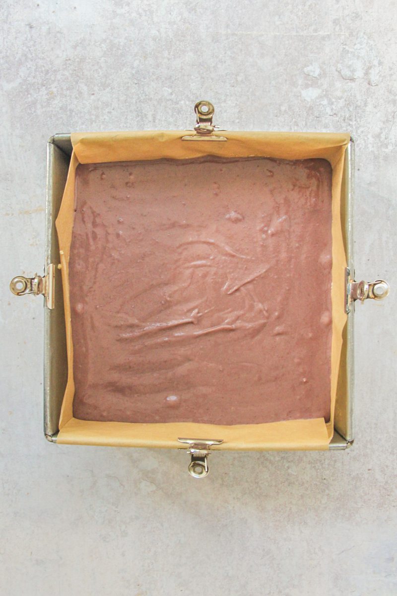 Unbaked sweet potato pie bars sits in a parbake pie crust in a square metal baking dish on a gray surface.