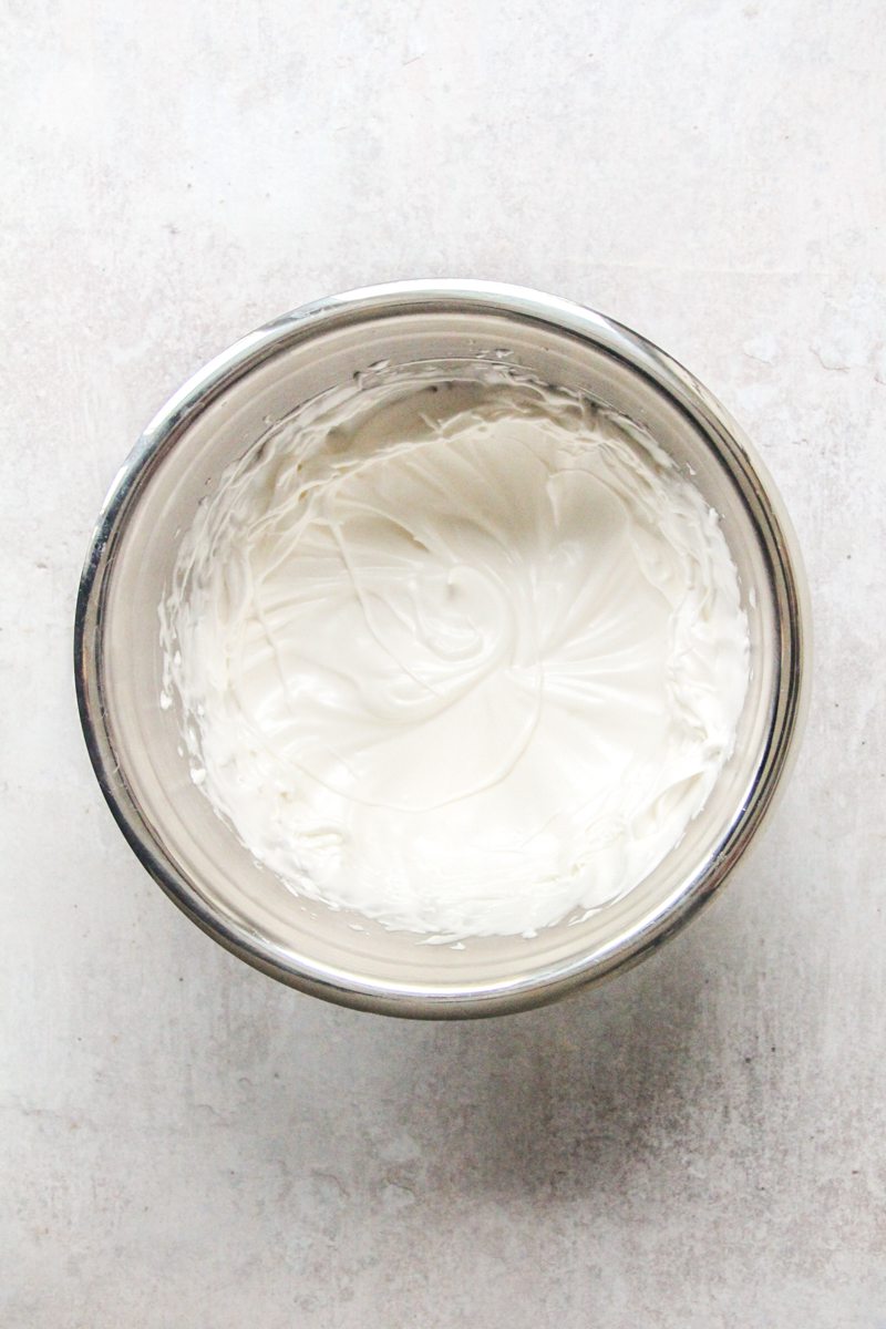 Whipped marshmallow meringue sits in a stainless steel bowl on a gray surface.