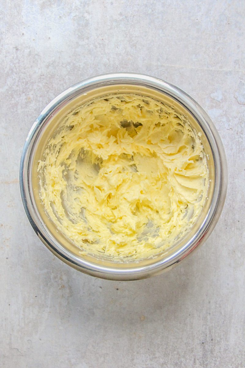 Whipped butter and sugar sits in a stainless steel bowl on a gray surface.