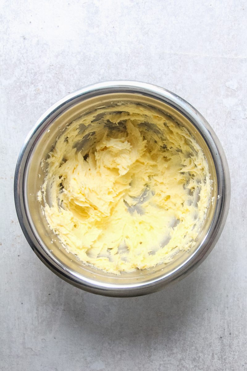 Whipped butter and sugar sits in a stainless steel bowl on a gray surface.