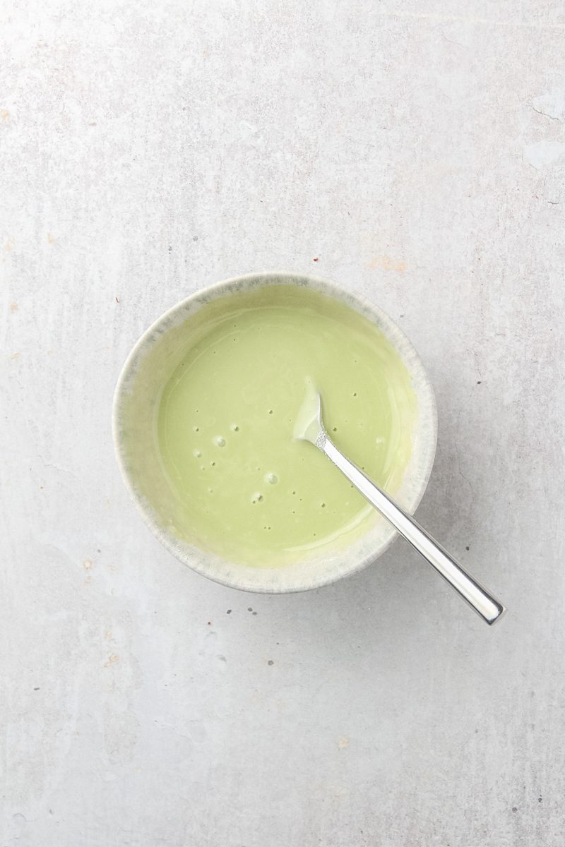 Peppermint icing sits in a blue ceramic bowl on a gray surface.