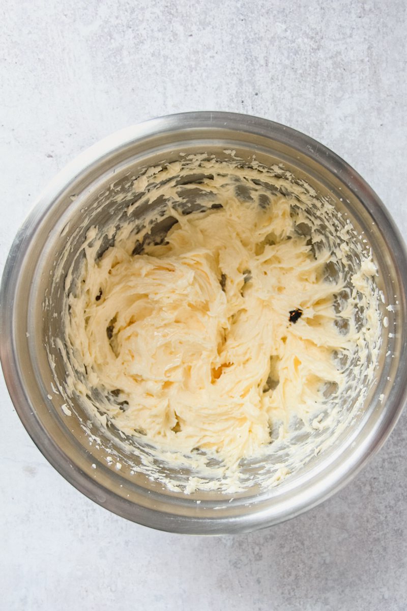 Whipped sugar and butter sit in a stainless steel bowl on a gray surface.