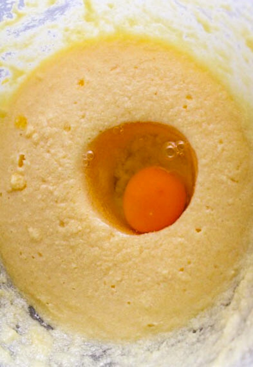 An egg sits in the center of a whipped butter and sugar mixture in a bowl.
