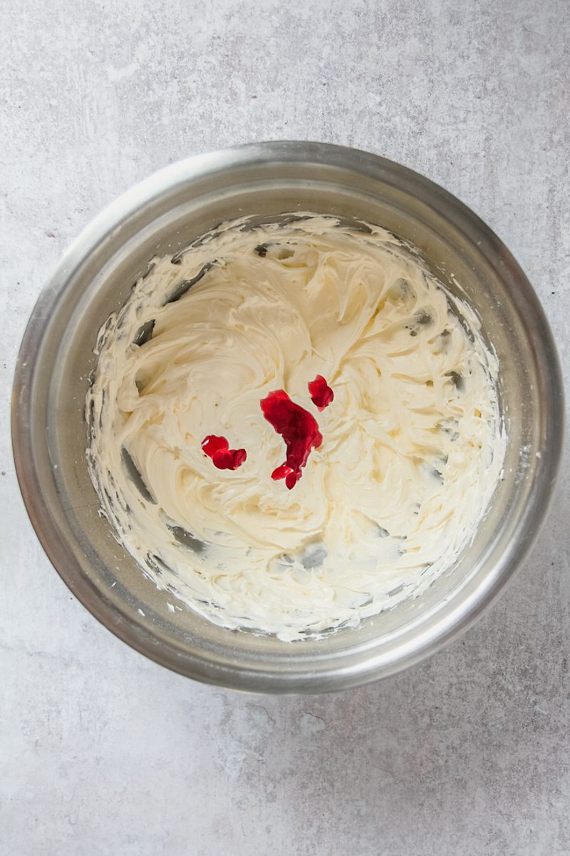 Whipped buttercream with raspberry jam on top sits in a stainless steel bowl on a gray surface.