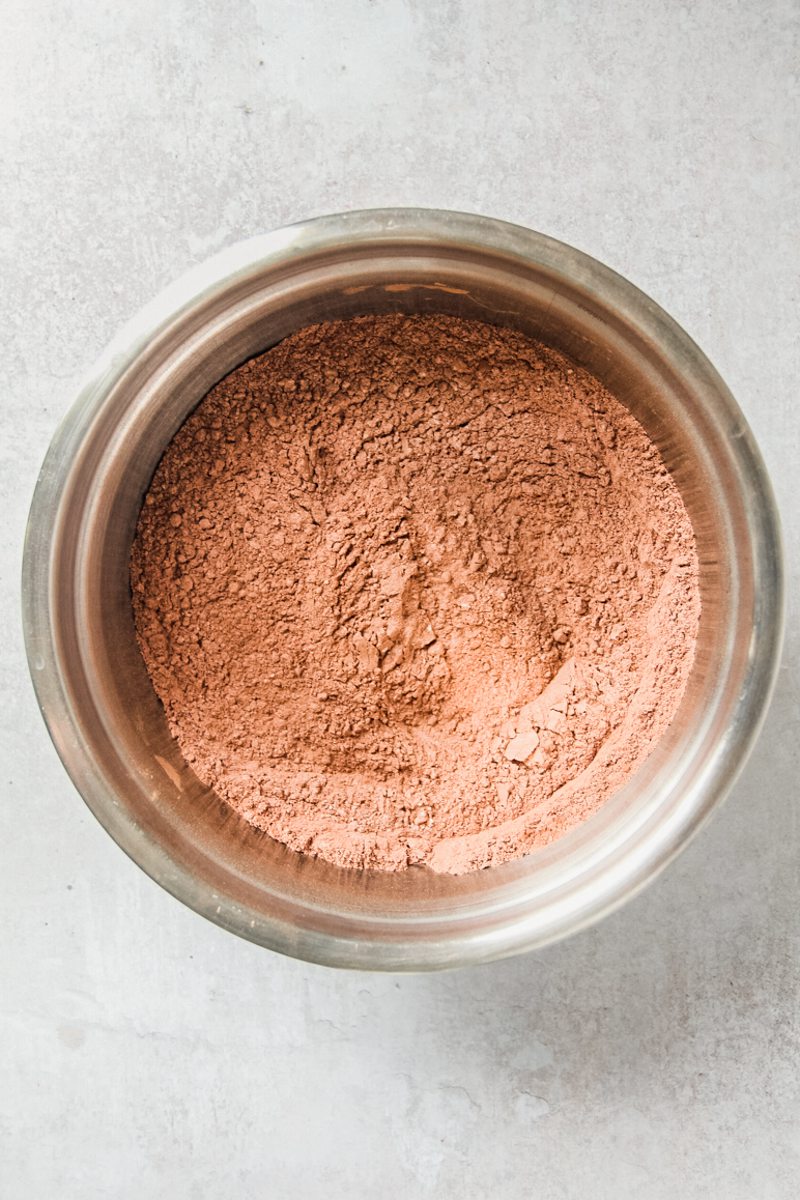 A cocoa powder mixture sits in a stainless steel bowl on a gray surface.