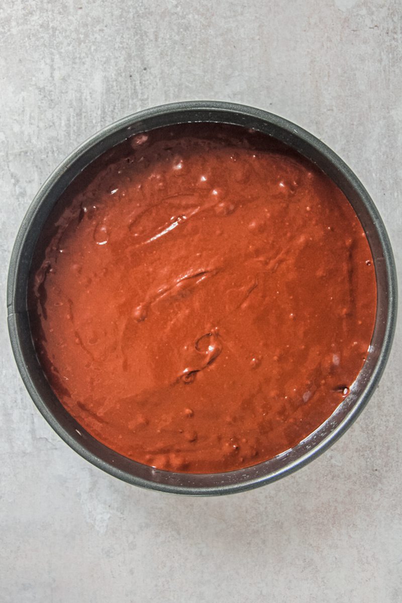 Buttermilk chocolate cake batter sits in a round metal baking tin on a gray surface.