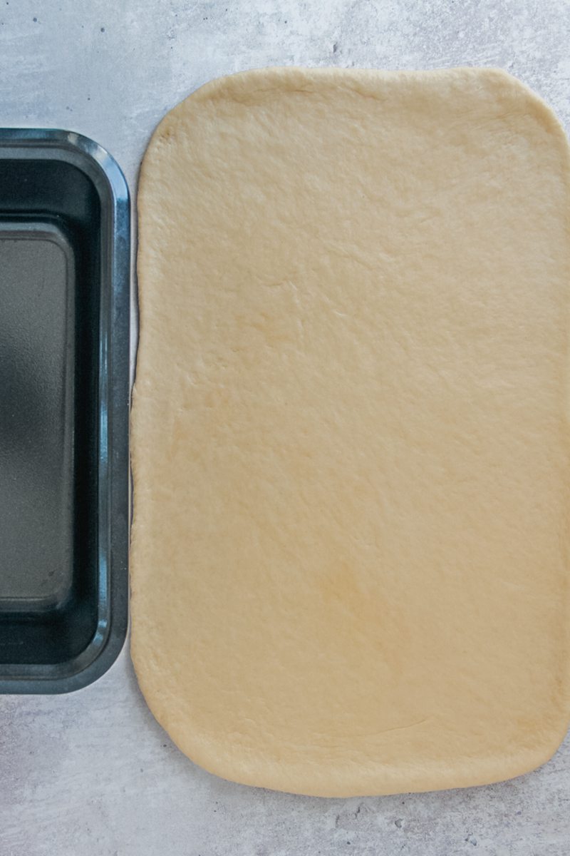 Rolled out babka dough rectangle sits next to a metal loaf tin on a gray surface.