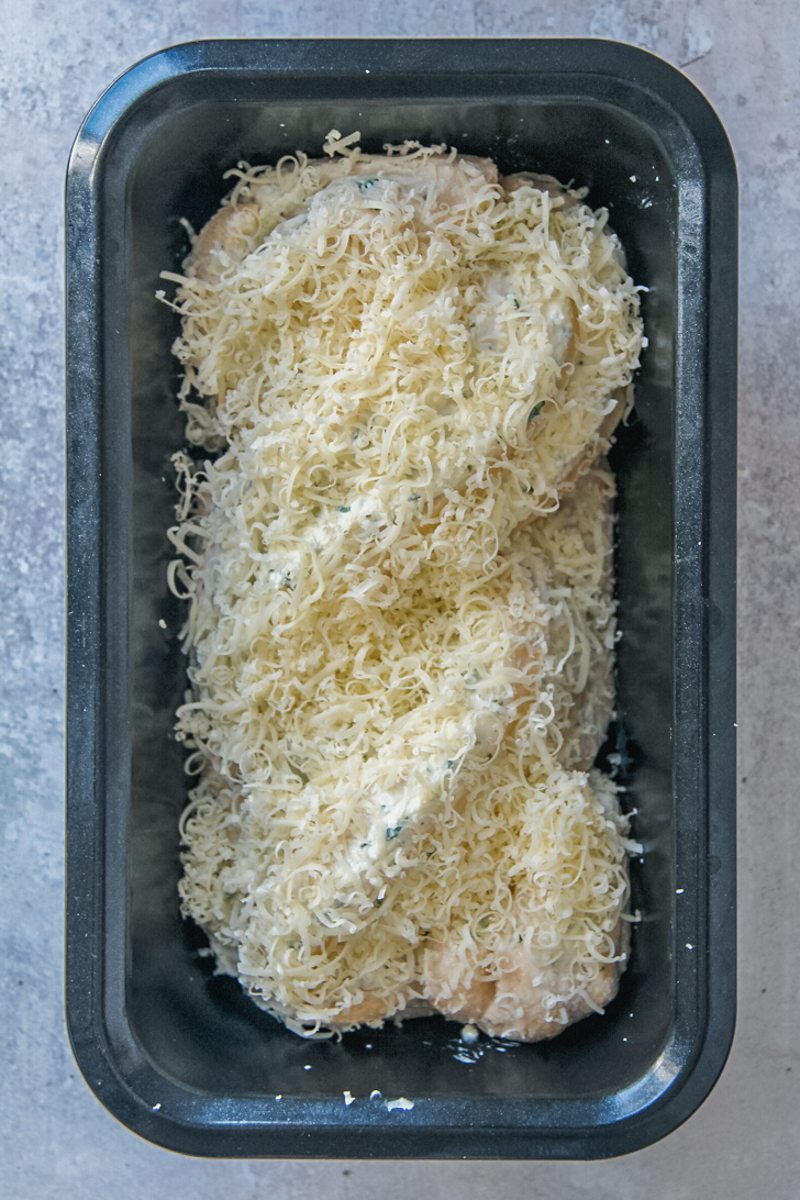 Finely grated cheese sits on top of unbaked babka in a metal loaf tin on a gray surface.