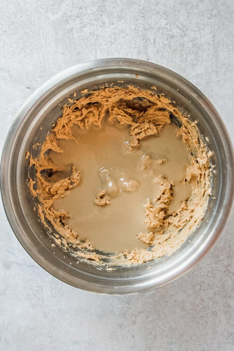 Tahini sits on top of whipped cookie butter in a stainless steel bowl on a gray surface.